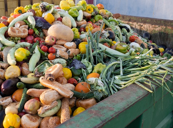 A large metal dumpster hold a mound of wasted food like baked items, vegetables and fruit.